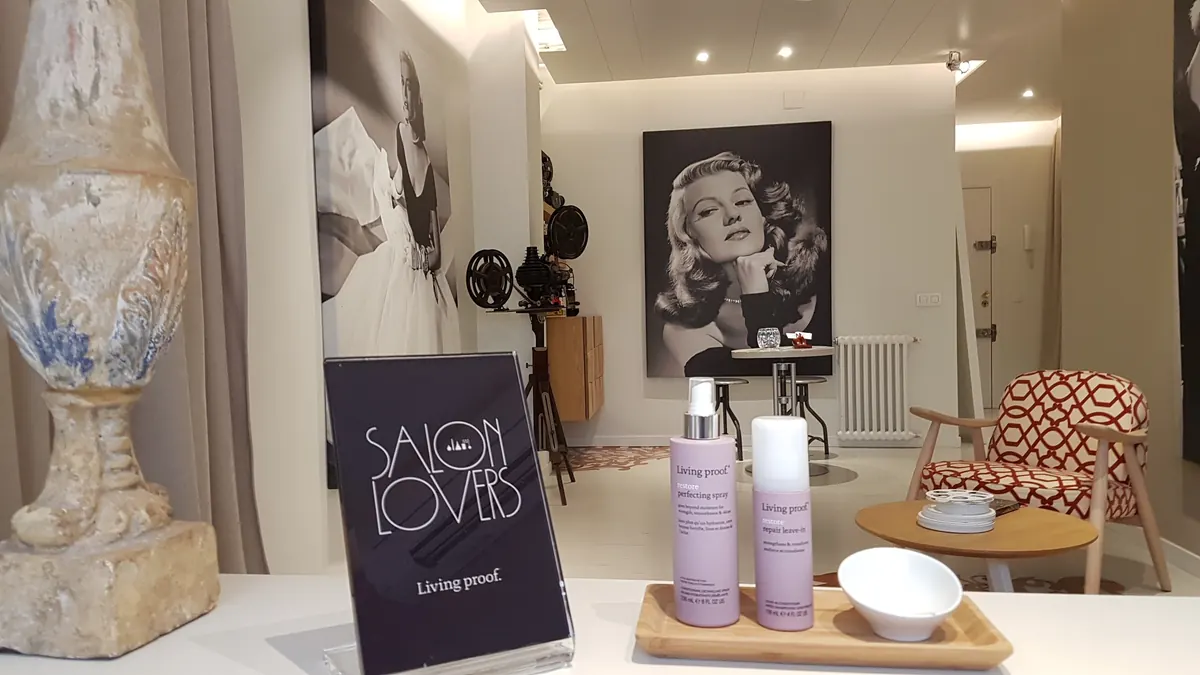 Productos Living Proof y cartel "Salon Lovers" en el estudio; al fondo, retrato de Rita Hayworth